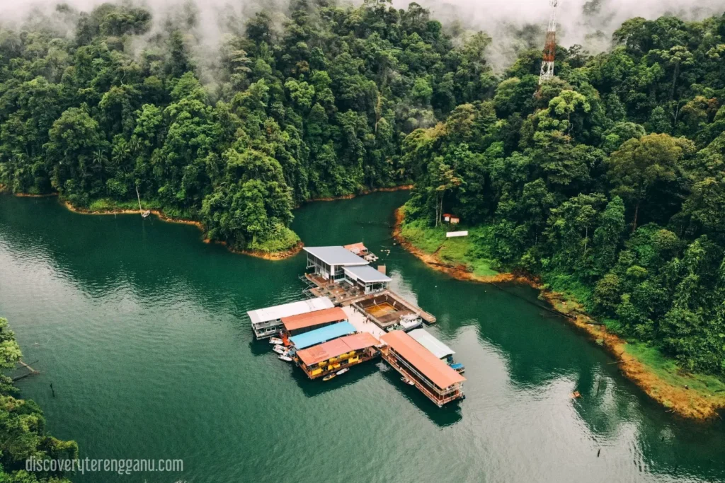Pandangan udara Tasik Kenyir: air hijau di celah hutan berkabus dengan deretan houseboat berlabuh di pelantar terapung