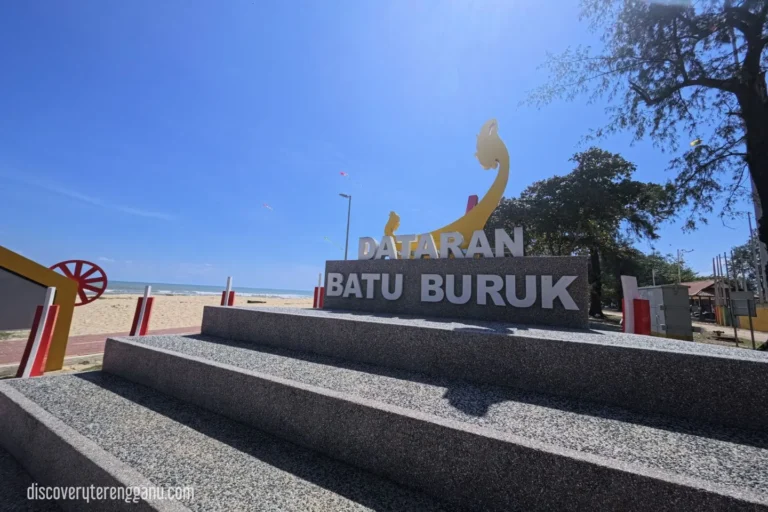 Tangga konkrit dan papan tanda besar Dataran Batu Buruk dengan pantai dan langit biru di belakang