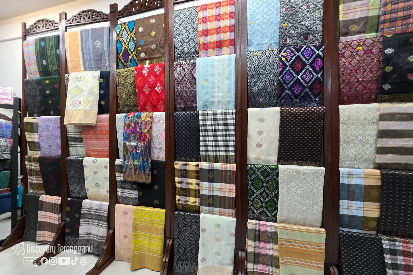 Rak kayu berukir dipenuhi kain songket dan sampin pelbagai corak dan warna di kedai kain Pasar Kedai Payang