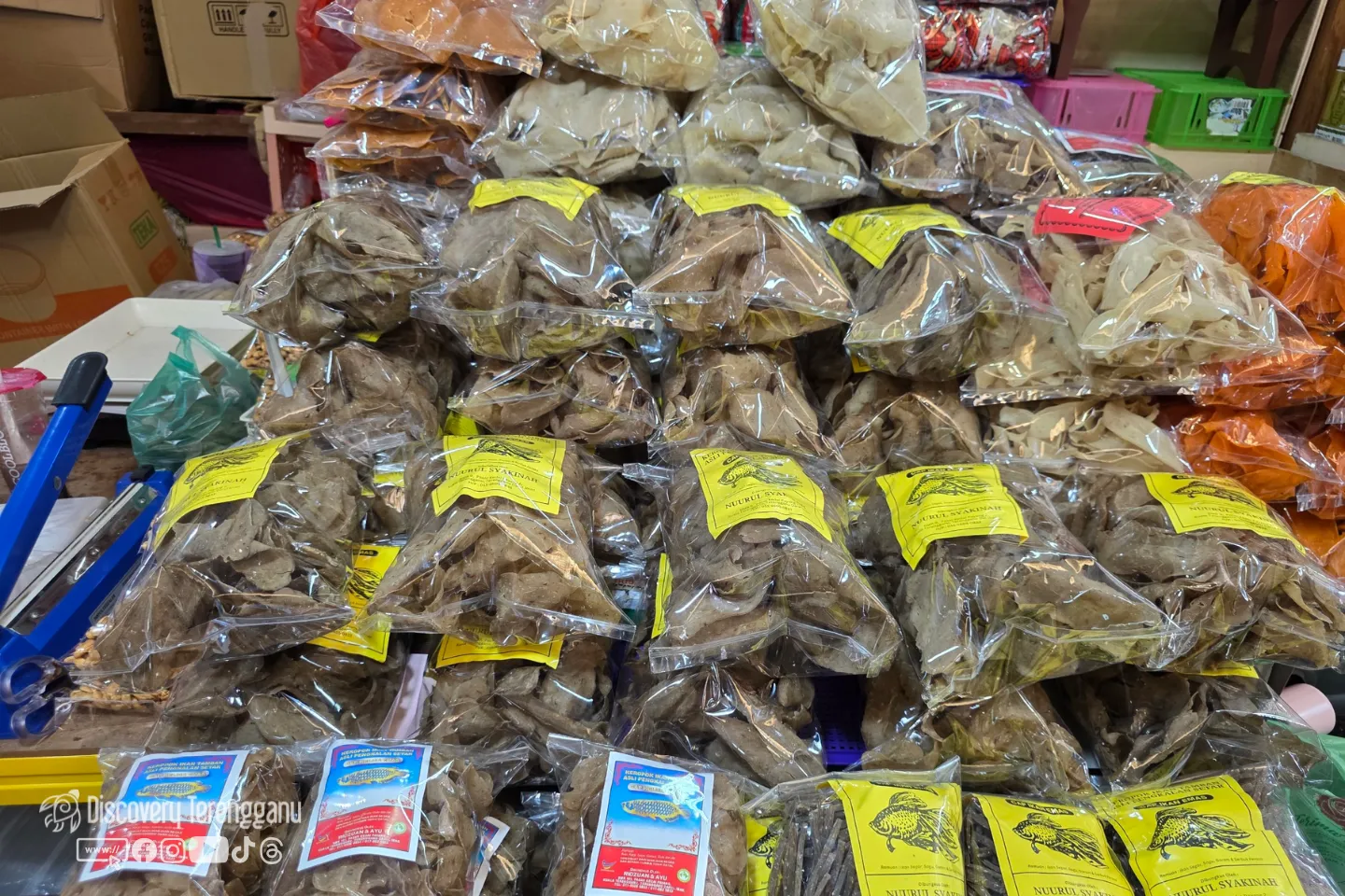 Bungkusan keropok keping bertimbun di kaunter kedai, sebahagiannya berlabel dan sedia dibungkus dengan mesin pengedap