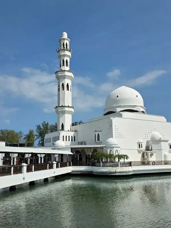 Masjid Tengku Tengah Zaharah berwarna putih dengan menara tinggi dan kubah, di tepi air pada waktu siang