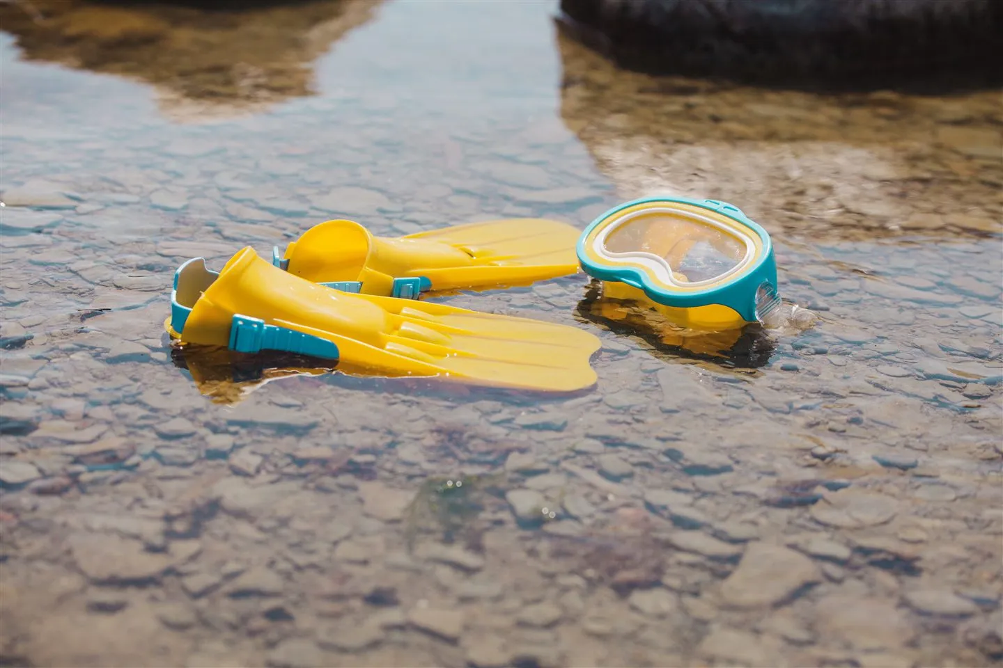 Kaki katak kuning dan cermin snorkeling biru-kuning di atas permukaan air cetek yang jernih