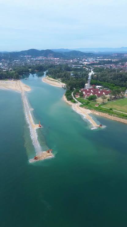 Pandangan udara Muara Sungai Ibai, Kuala Terengganu: sungai berwarna hijau kebiruan mengalir ke laut di antara dua beting pasir, dengan jentera di hujung tambak batu serta bandar dan bukit di latar belakang