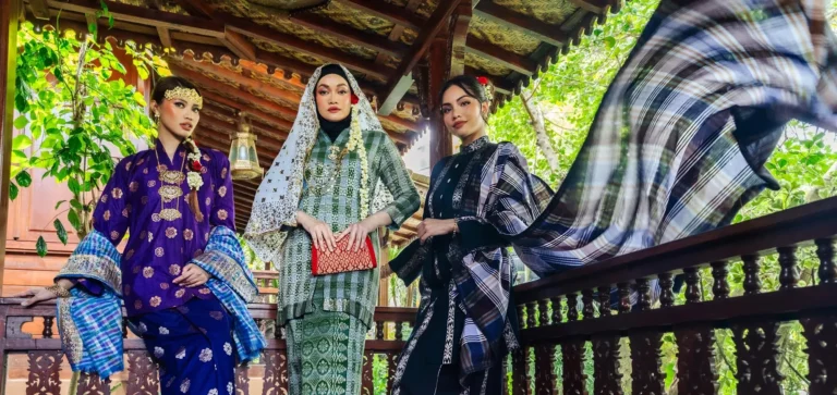Tiga wanita memperagakan busana dan selendang songket Terengganu di rumah tradisional Melayu